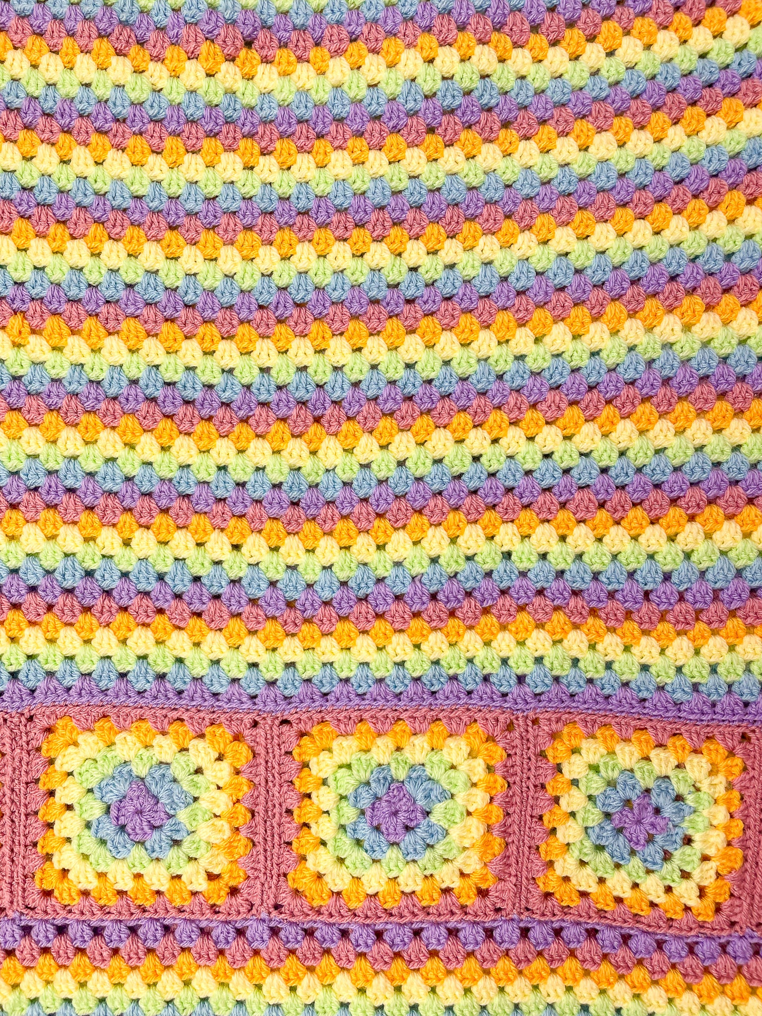 Close view of a rainbow striped skirt in pastel colours with a granny square design at the bottom showing the crochet stitches.