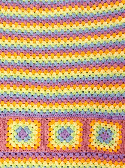 Close view of a rainbow striped skirt in pastel colours with a granny square design at the bottom showing the crochet stitches.