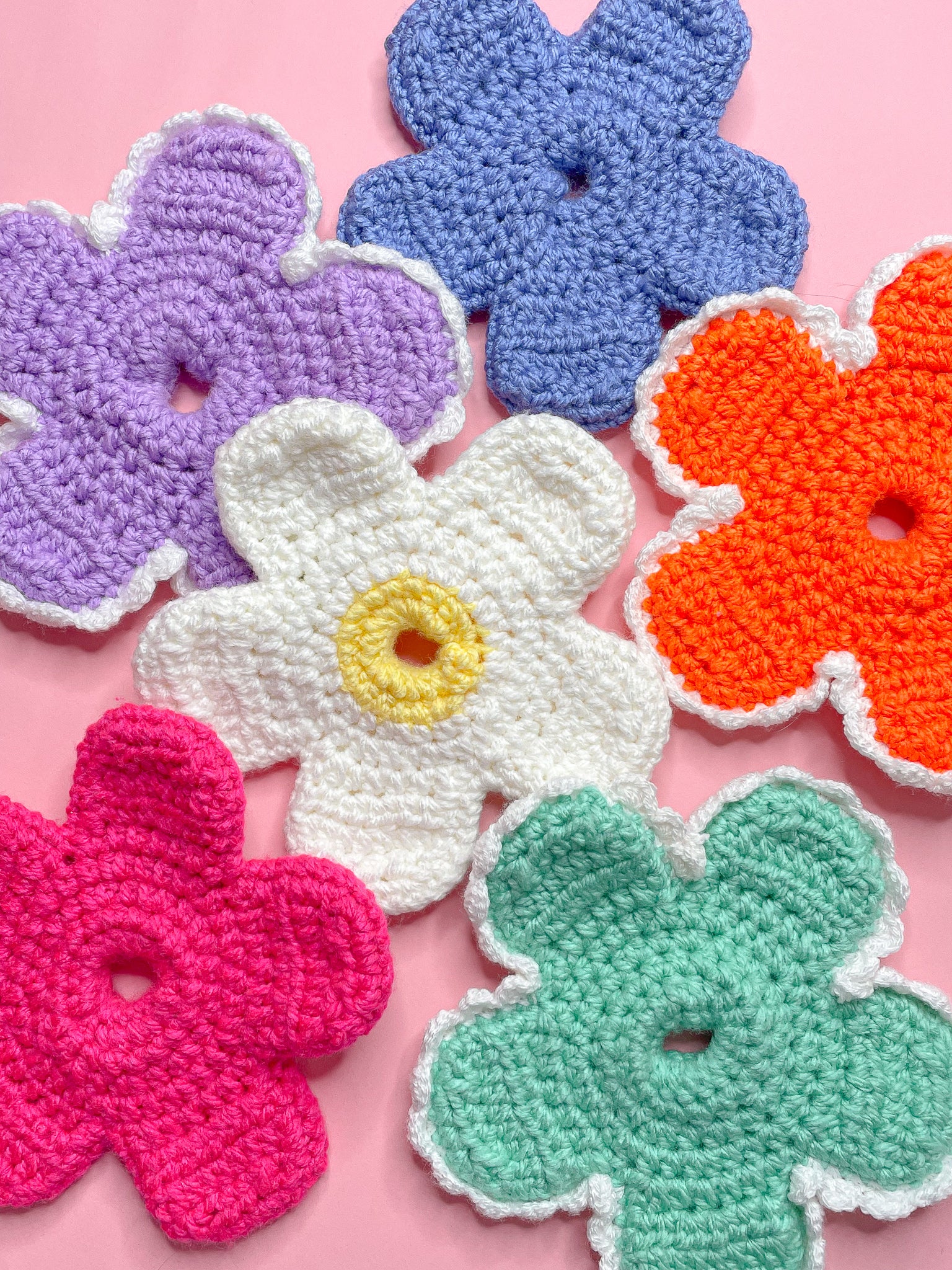 Six daisy shaped scrunchies in multiple colours lying together on a pink background.