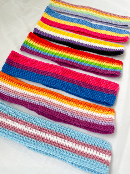 Flat lay of seven crochet headbands all in different pride flag colours lying flat on a white background.