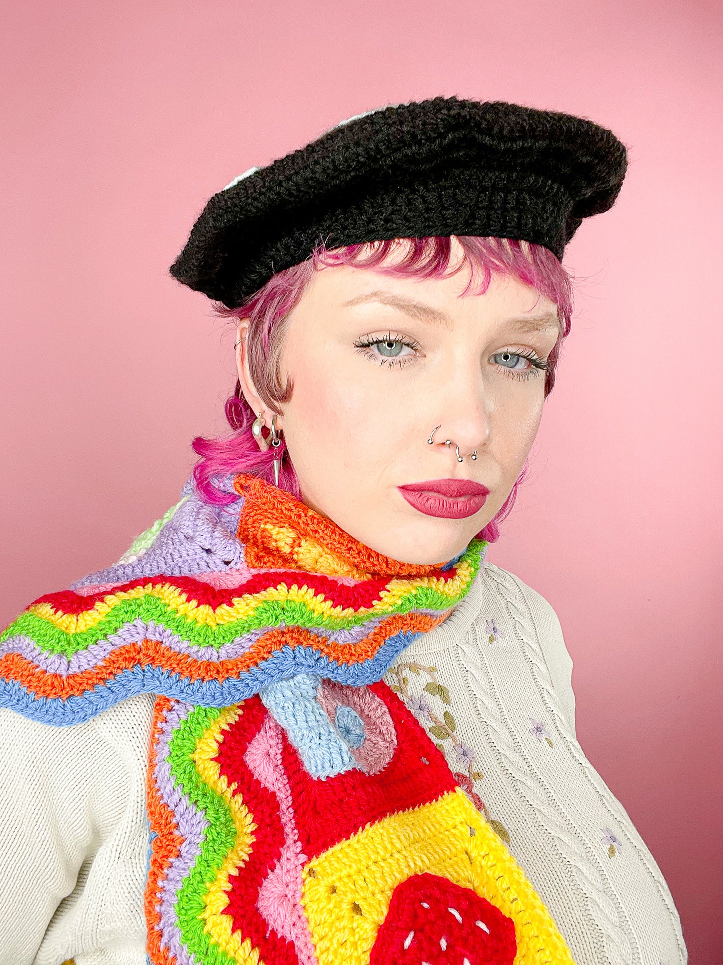 Close view of a woman posing wearing a black crochet beret and a multicoloured scarf.