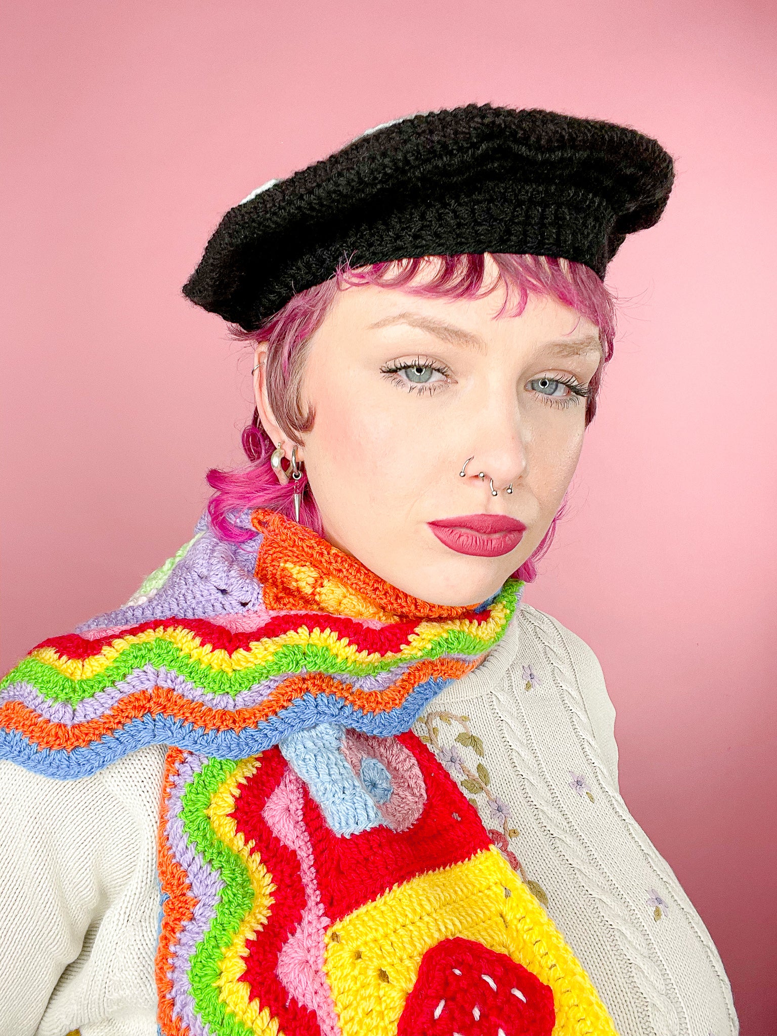 Close view of a woman posing wearing a black crochet beret and a multicoloured scarf.