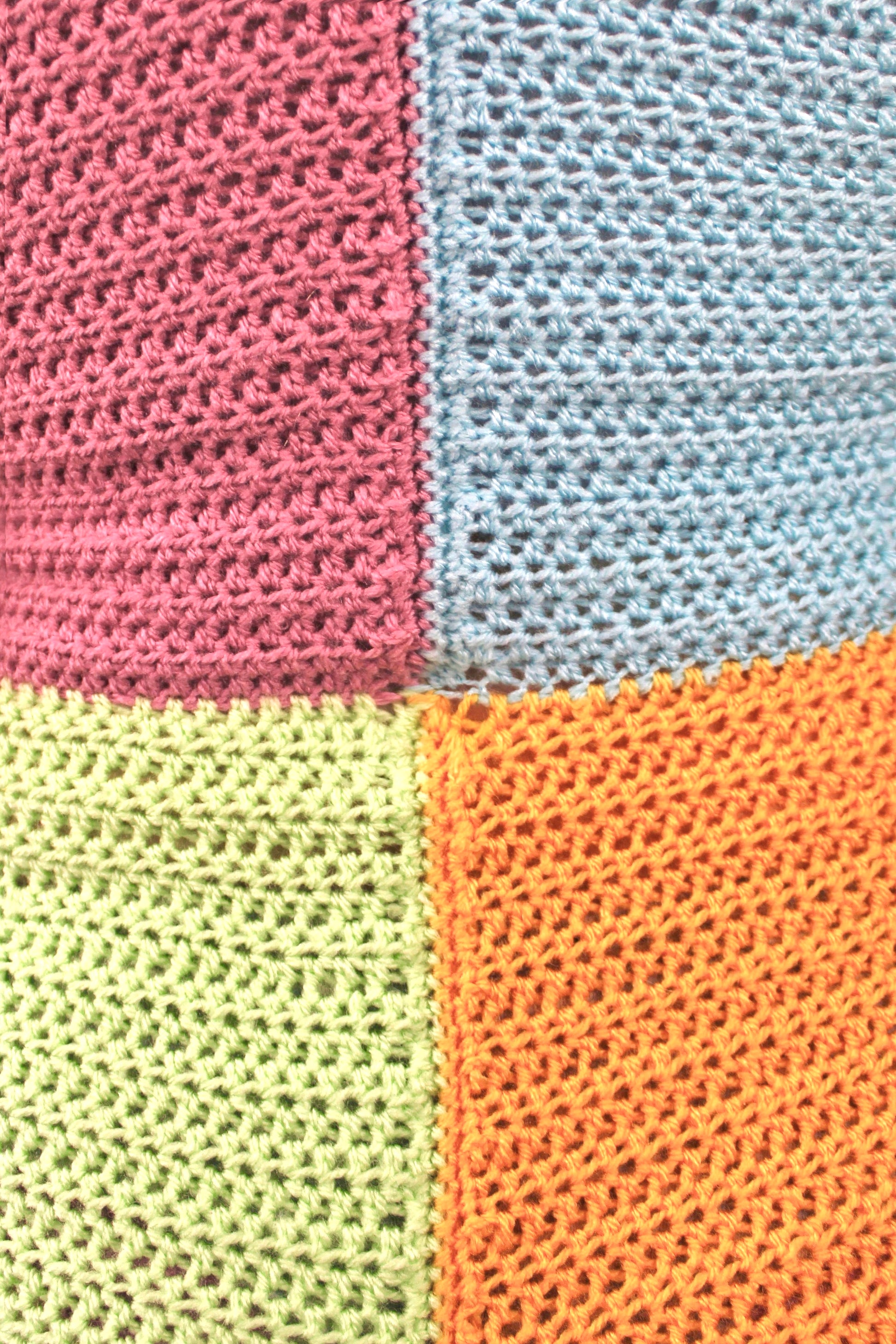 Close view of a playsuit with a pastel patchwork design, pale pink in the top left, baby blue in right, mint green in bottom left and pale orange in the right showing the crochet stitches.