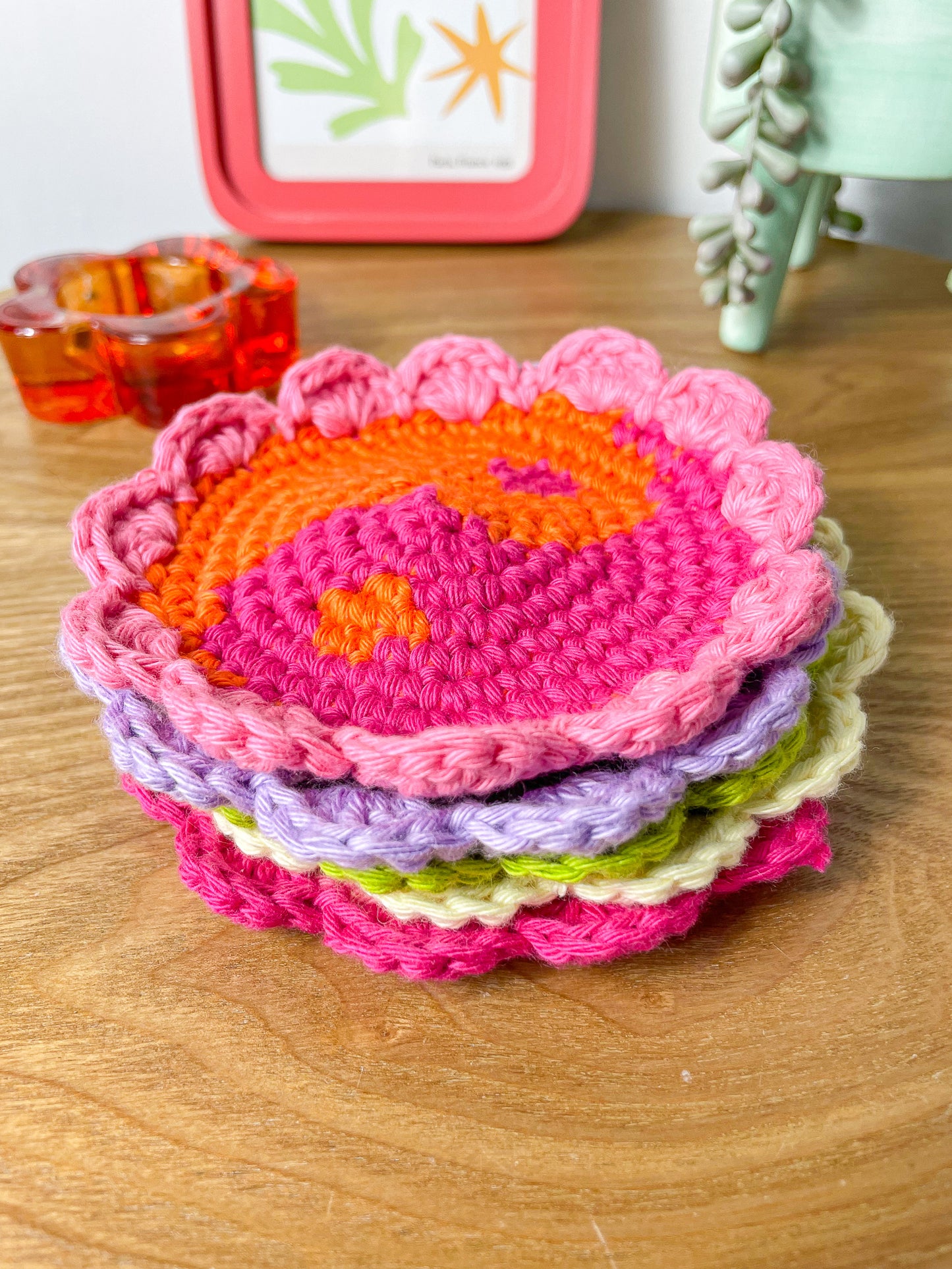 Five yin and yang style coasters stacked on top of each other, the top one with an orange and bright pink centre and pink ruffled edges, lying on a wooden table.