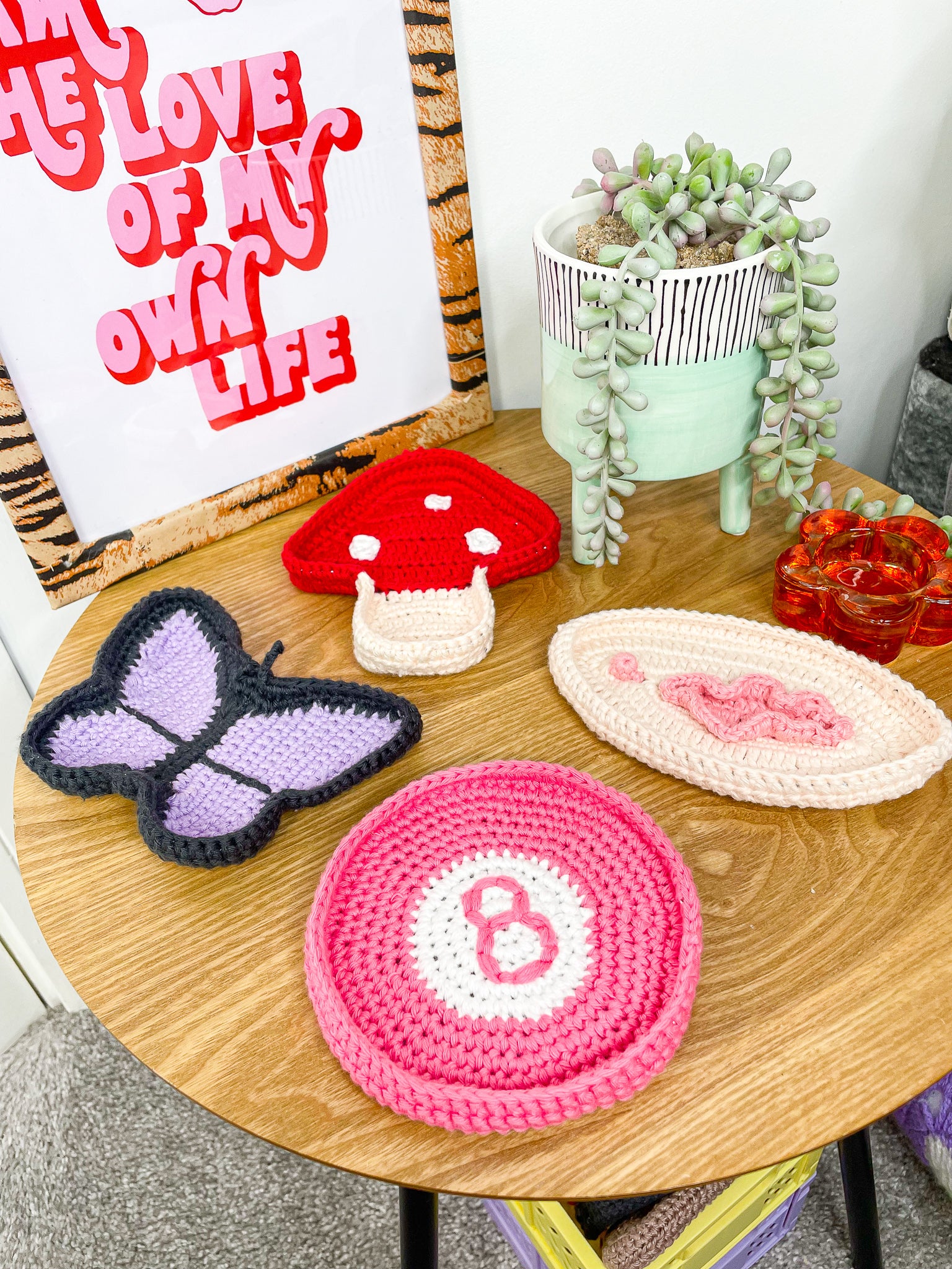 Four ring trays shaped like a mushroom, butterfly, 8 ball and vulva, lying together on a wooden side table with decor around.