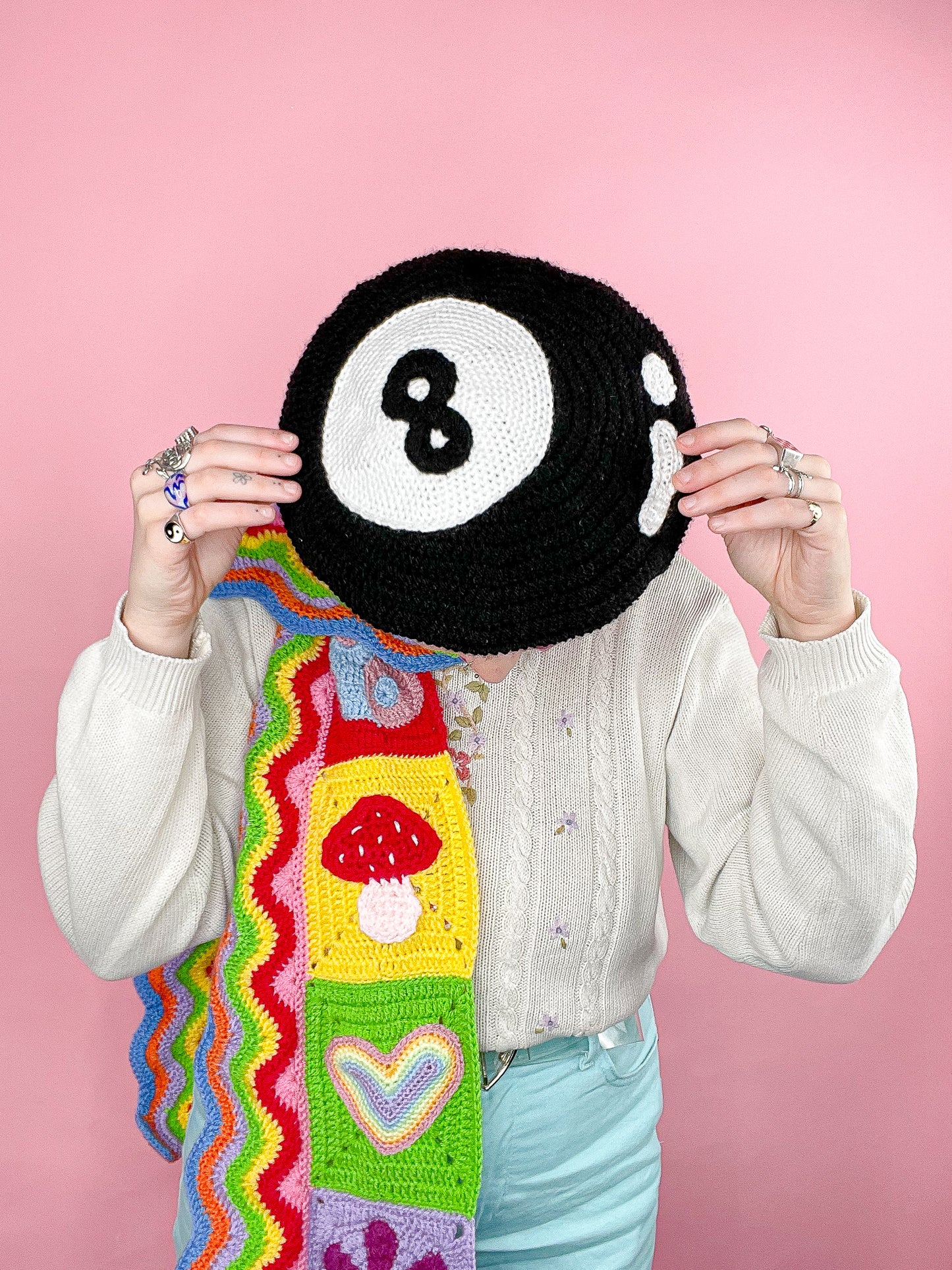 Above view of woman posing wearing a crochet beret in black resembling an eight ball with a multicoloured scarf and granny style jumper.