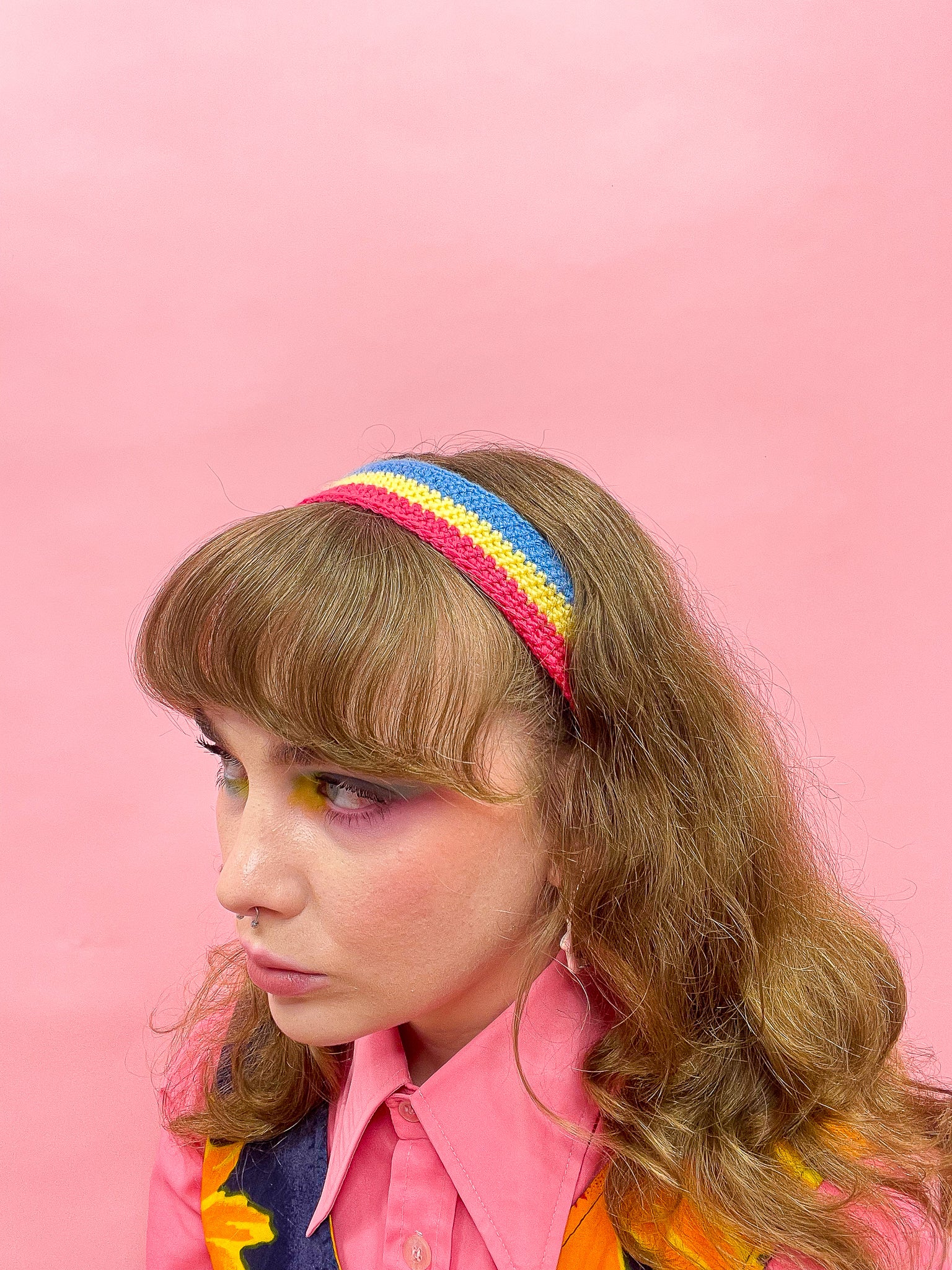 Side above view of woman wearing a crochet headband in the pansexual flag colours (pink, yellow, blue), wearing a pink shirt and blue and yellow dress.