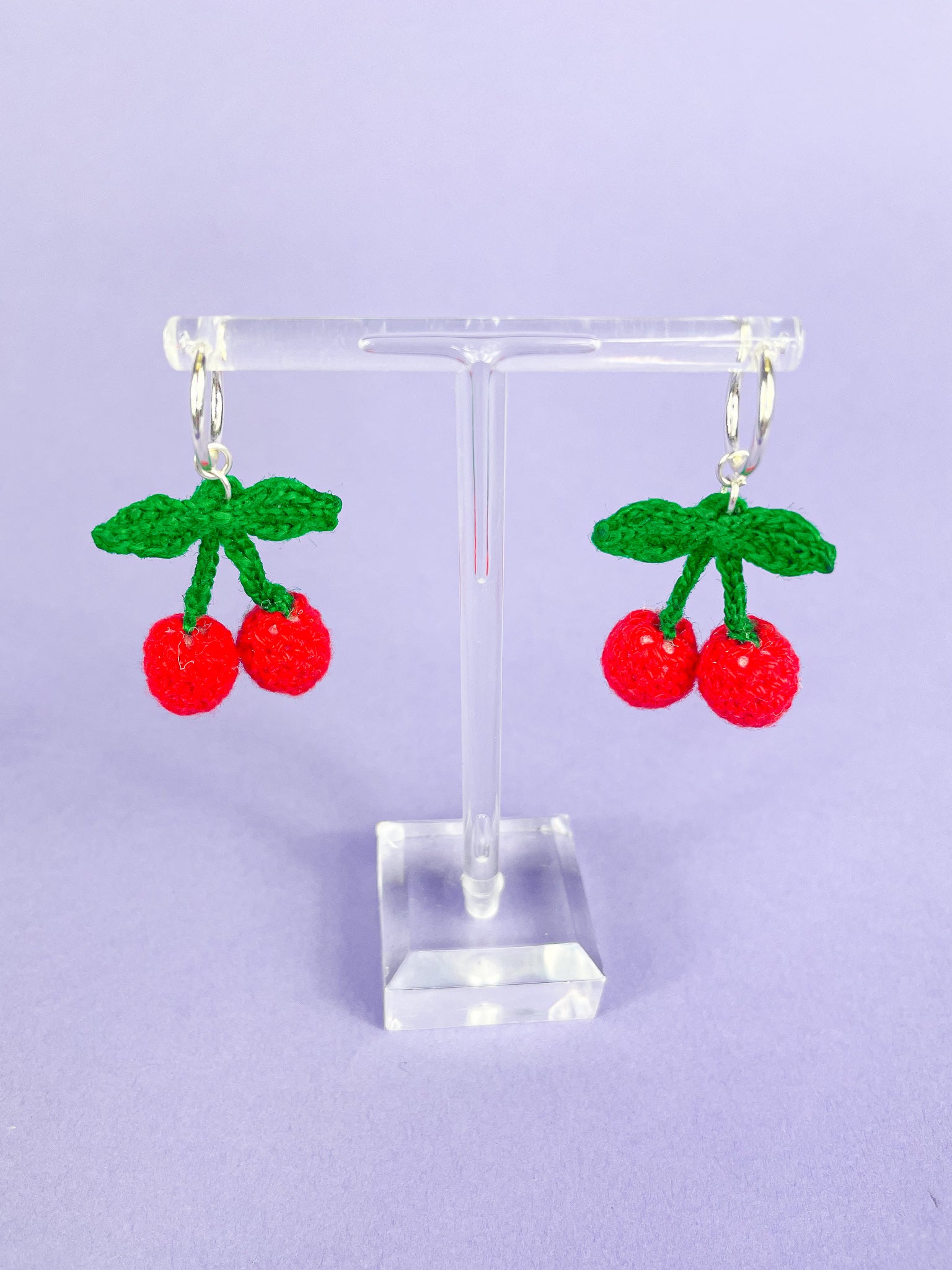 Above view of a pair of crocheted cherry earrings attached to hoops hung up on an earring stand.