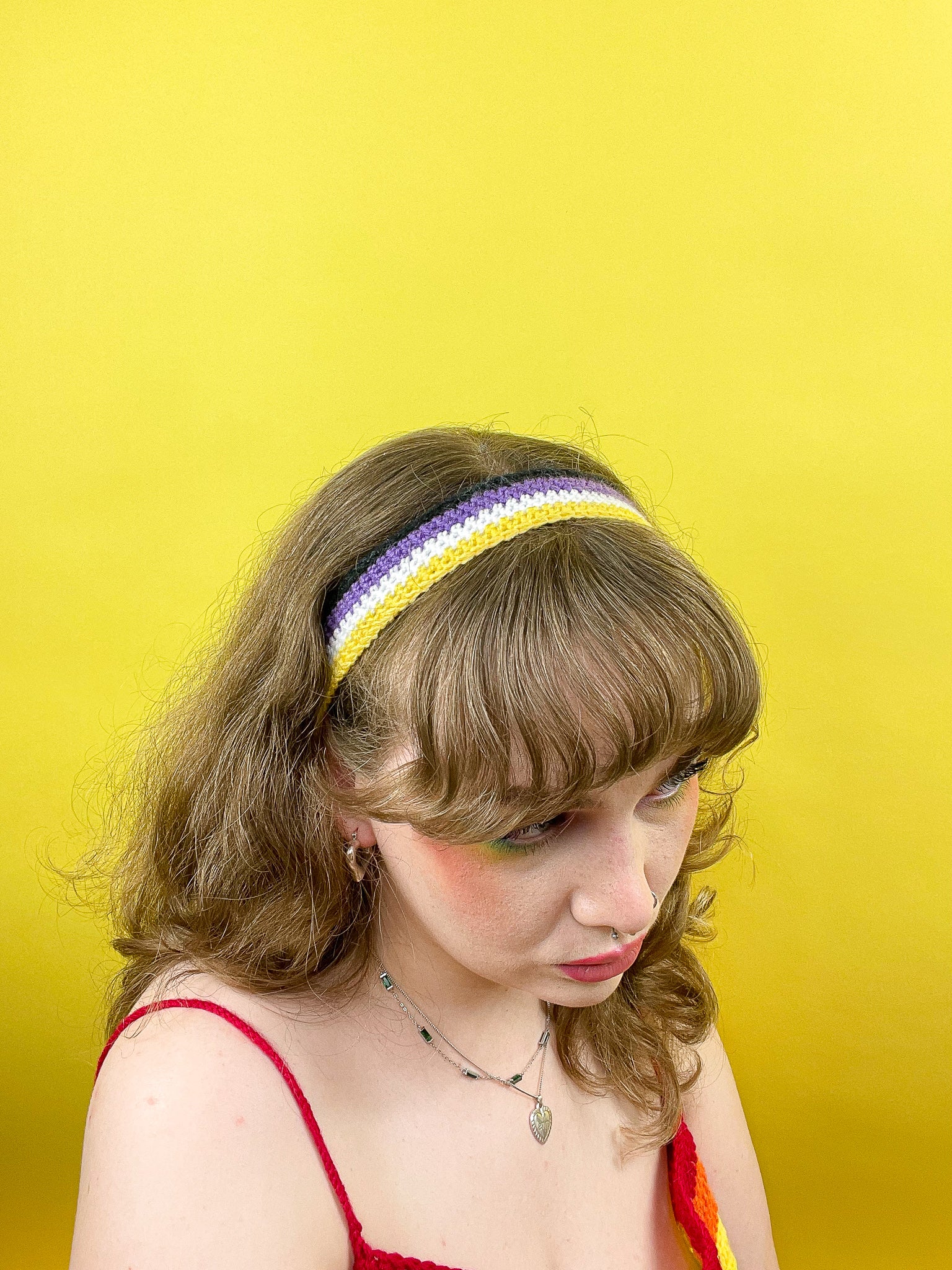 Above view of a woman wearing a crochet headband resembling the non-binary flag colours (yellow, white, purple and black).