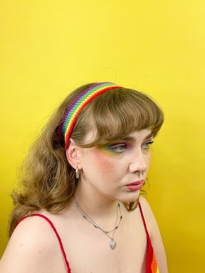 Side view of a woman wearing a bright rainbow headband with matching eyeshadow and a red crop top.