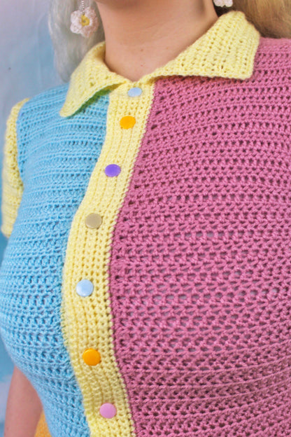 Close up of woman wearing a pastel patchwork playsuit with baby blue on one side and pale pink on the other with a pale yellow collar and multicoloured snap buttons on the polo.