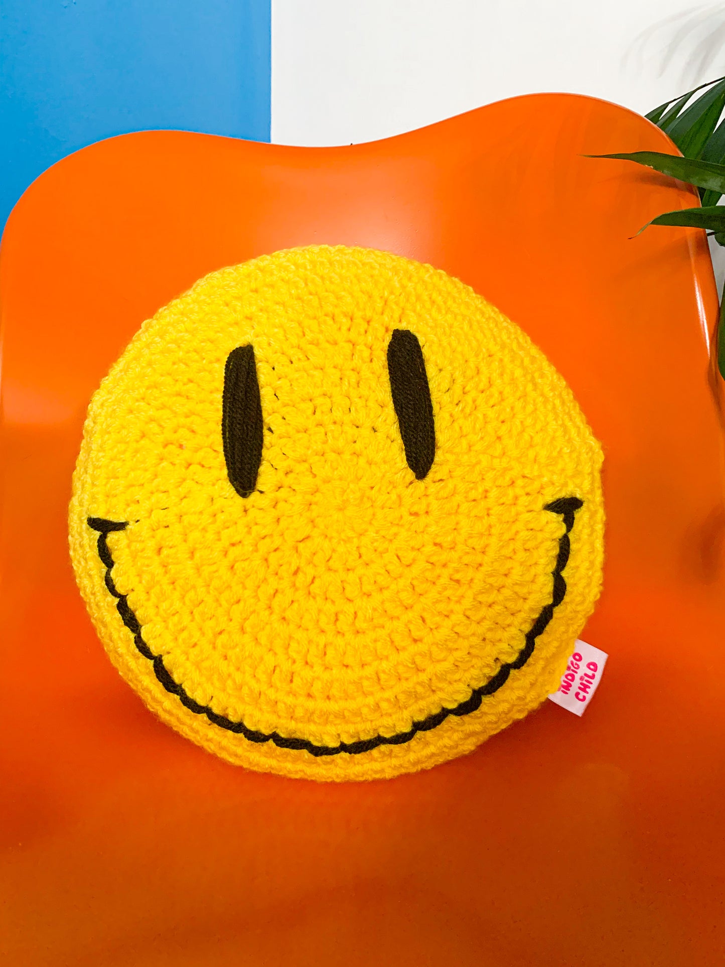 Close view of a yellow circle pillow with a hand stitched smiley face on the base sitting on an orange chair.