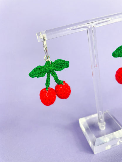 Close view of one crochet mini cherry earring hung on an earring stand.