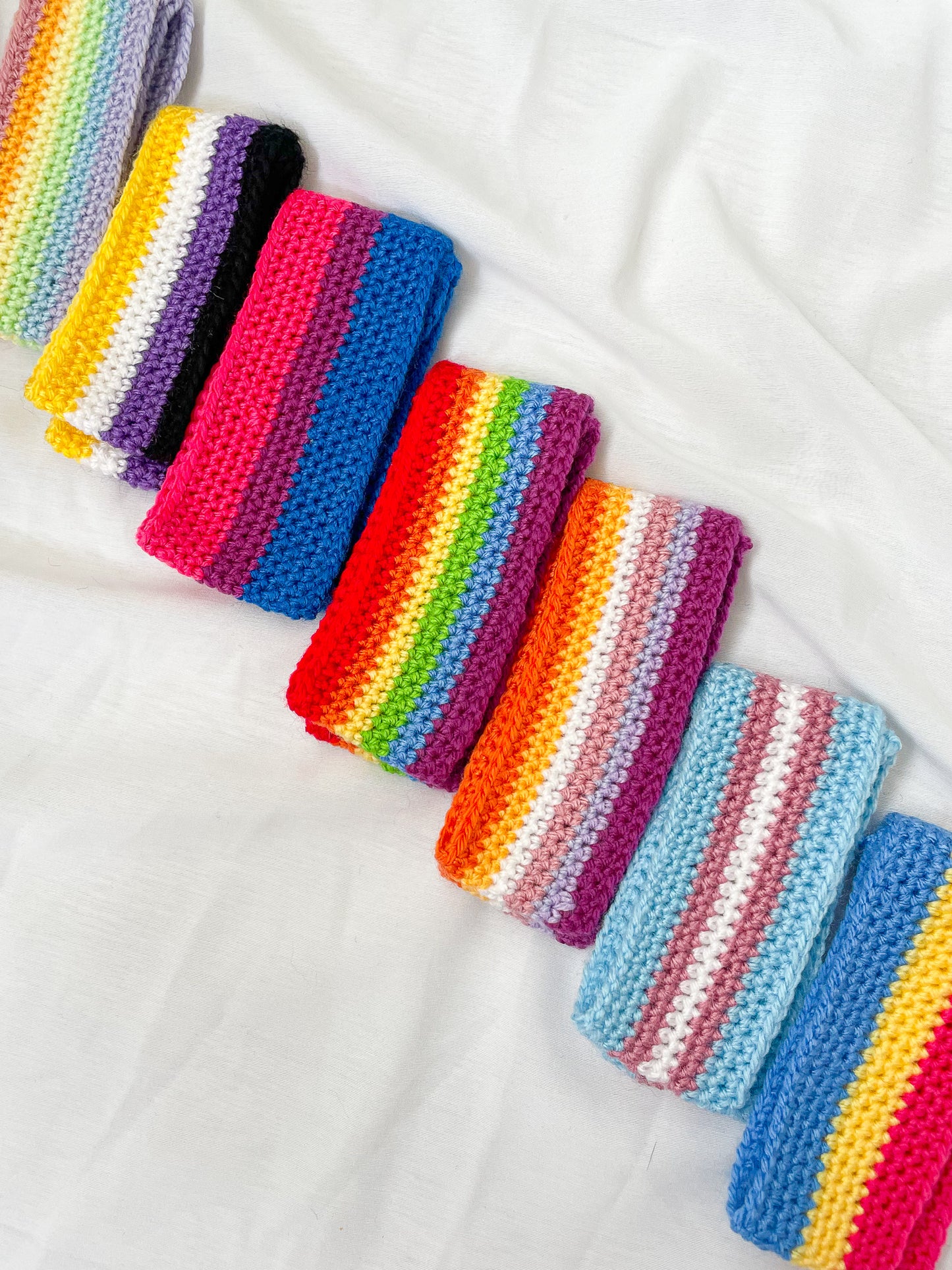 Flat lay of seven headbands in different pride flag designs folded in half lying next to each other in a row.