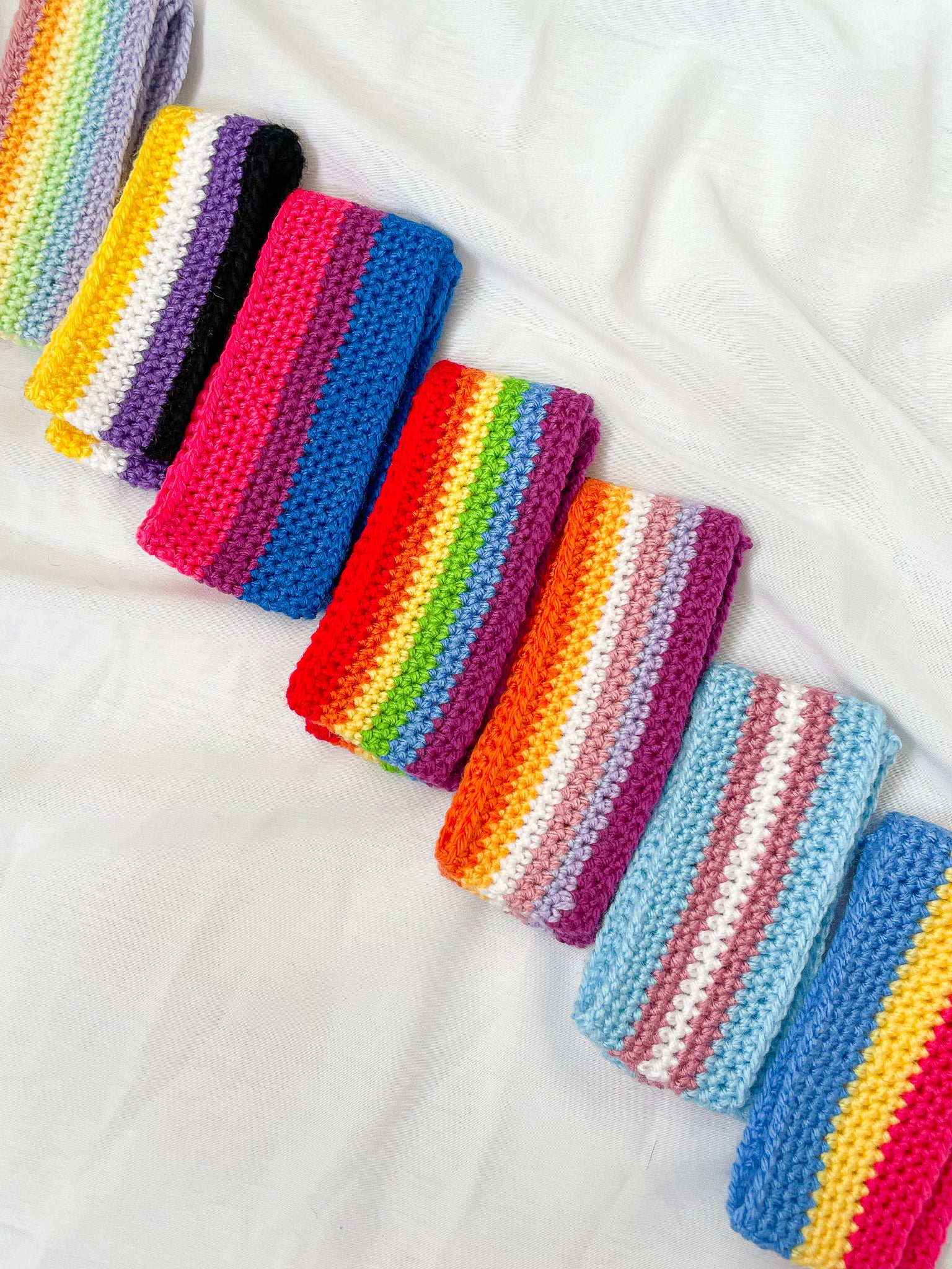 Flat lay of seven headbands in different pride flag designs folded in half lying next to each other in a row.