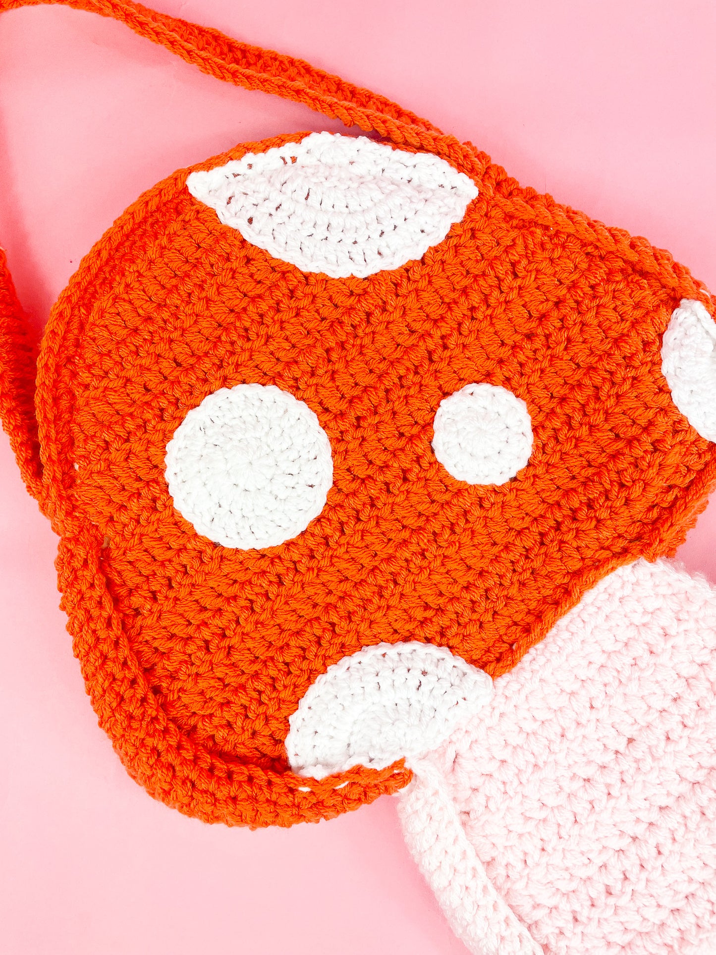 Close view of an orange mushroom shaped bag with white crochet appliqué dots to resemble a toadstool.