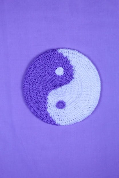 A purple and white beret with a yin and yang design lying on a purple background.