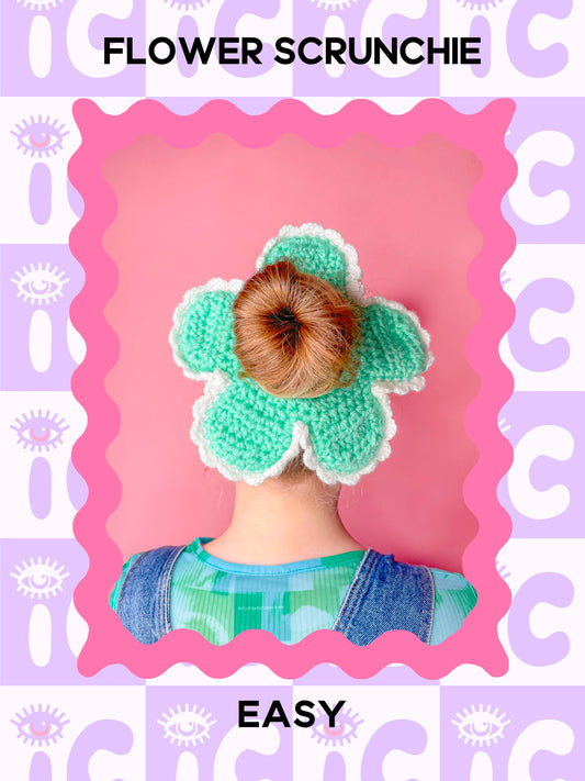 A pattern cover of a woman wearing a crochet scrunchie shaped like a flower in mint green with the words 'flower scrunchie' and the skill level 'easy' around the image.