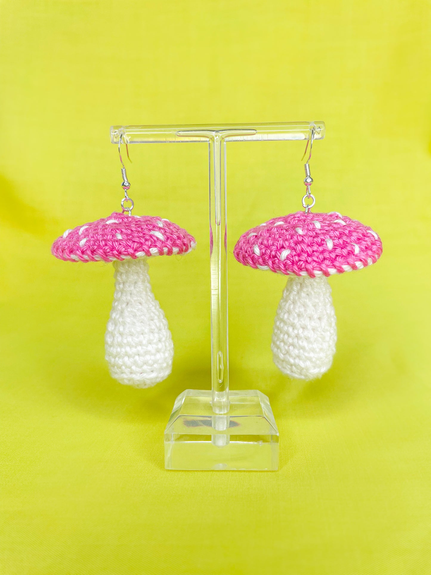 Pair of pink toadstool crochet earrings ganging on a clear earring stand.