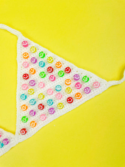 Close view of a white triangle cup bralette with happy face beads in various colours attached to it.