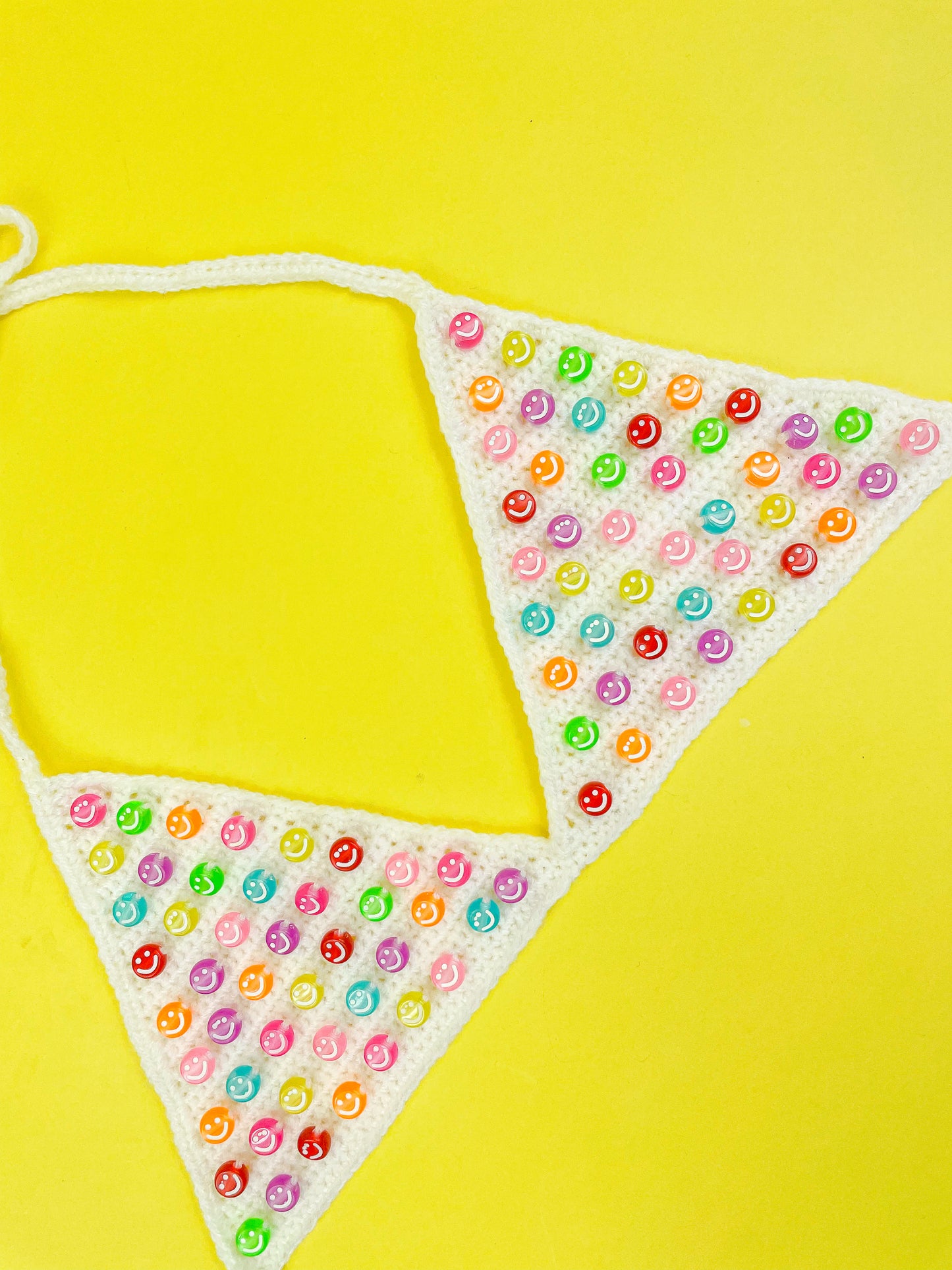 Side view of a beaded bralette in white with triangle cups lying flat on a yellow background.