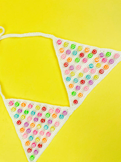 Side view of a beaded bralette in white with triangle cups lying flat on a yellow background.