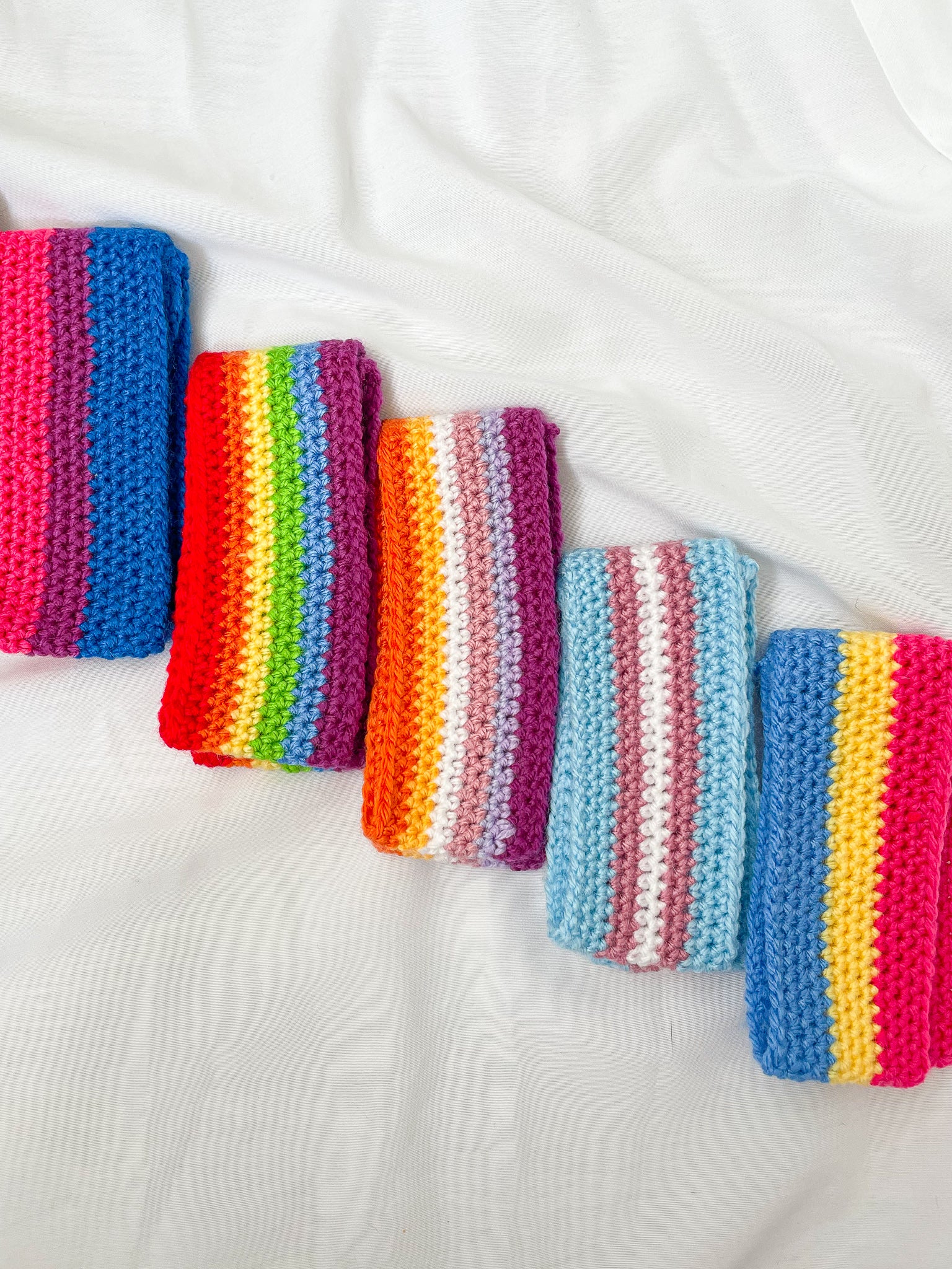 Flat lay of five headbands in different pride flag designs folded in half lying next to each other in a row.