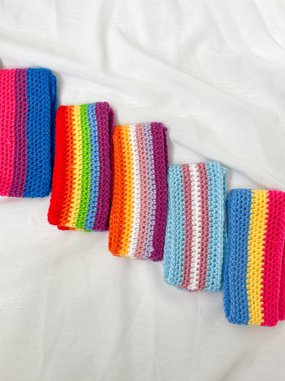 Flat lay of five headbands in different pride flag designs folded in half lying next to each other in a row.