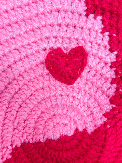 Close view of a crochet beret in pink and red with appliqué hearts sewn to it.