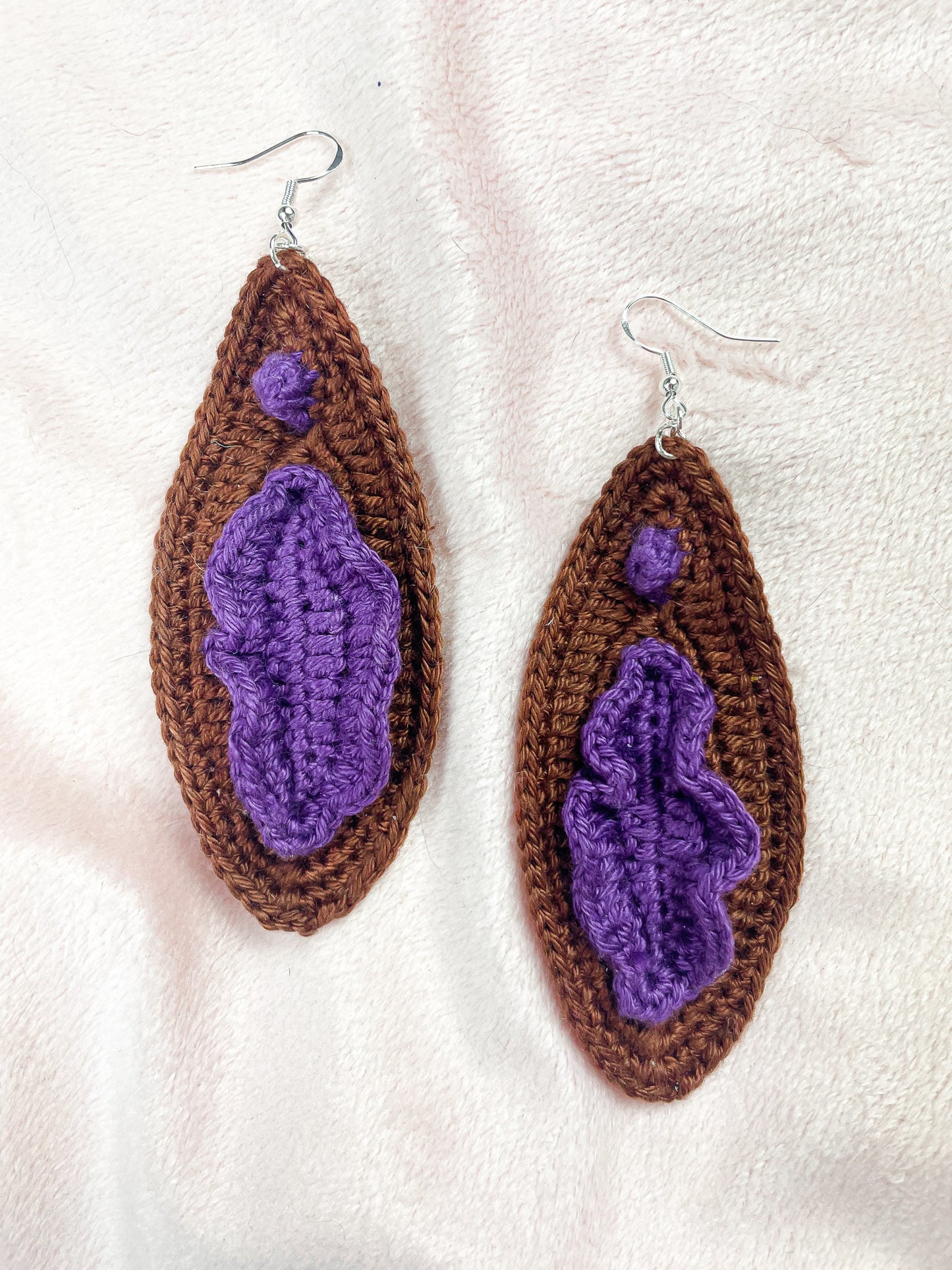 Close view of pair of dark brown earrings inspired by vulvas showing the crocheted stitches.