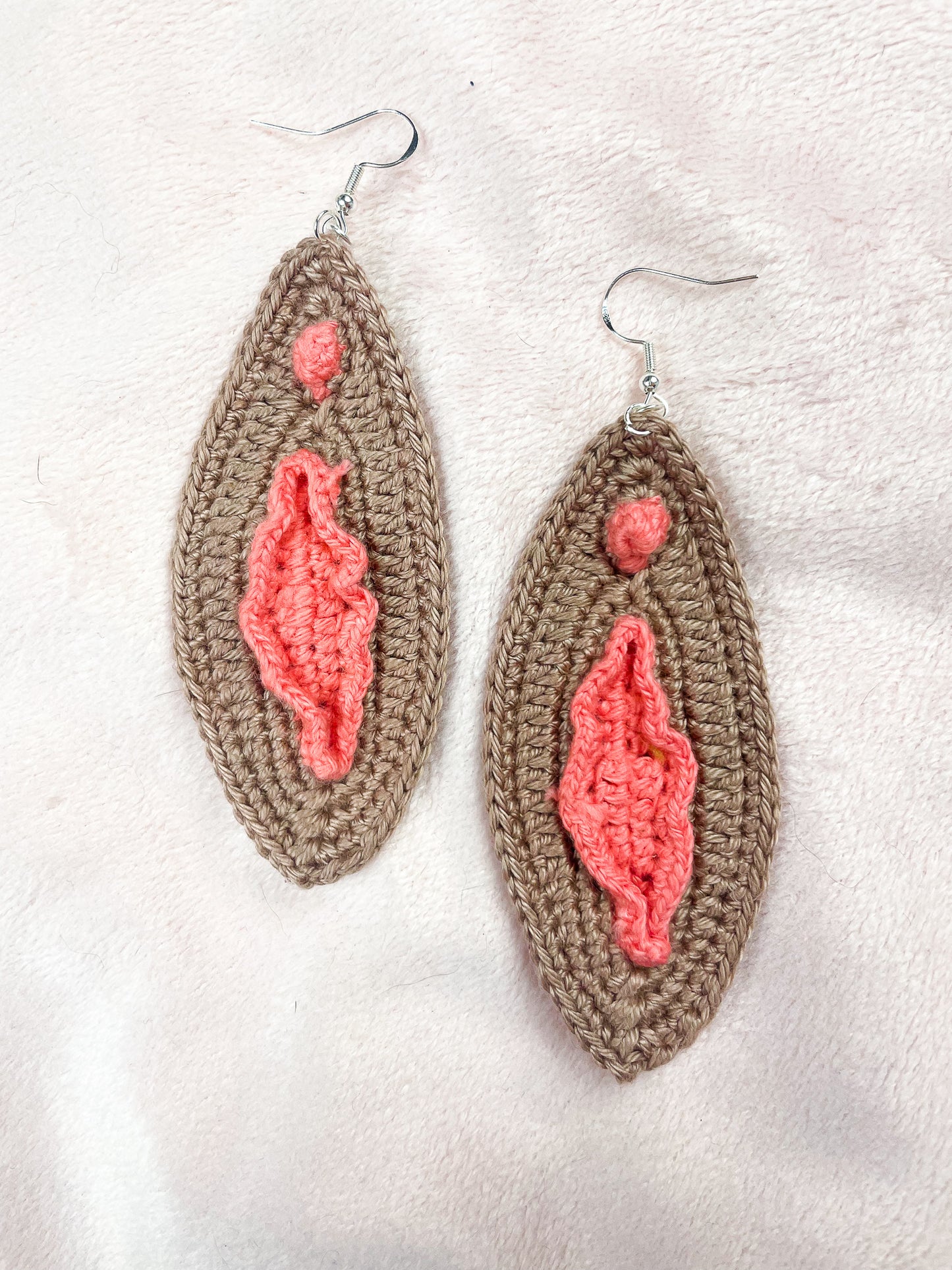 Close flat lay of a pair of brown and peach vulva inspired earrings with an oval shape and attached to silver butterfly hooks.