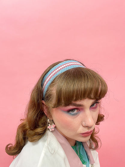 Above view of a woman wearing a crochet headband resembling the Trans flag colours with a matching outfit and makeup.