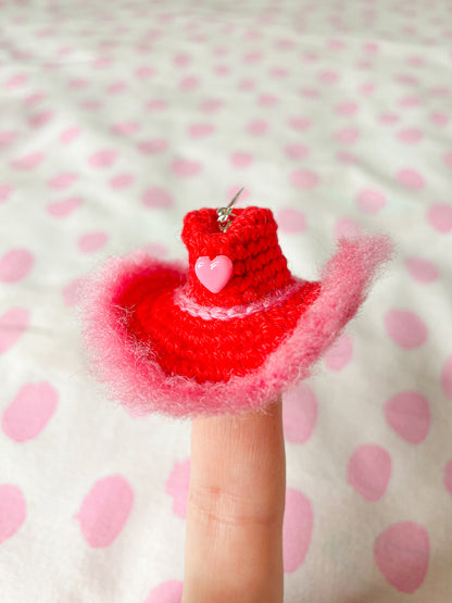 One cowboy shaped earring in red and pink sitting on top of someone's finger like it's wearing a hat.