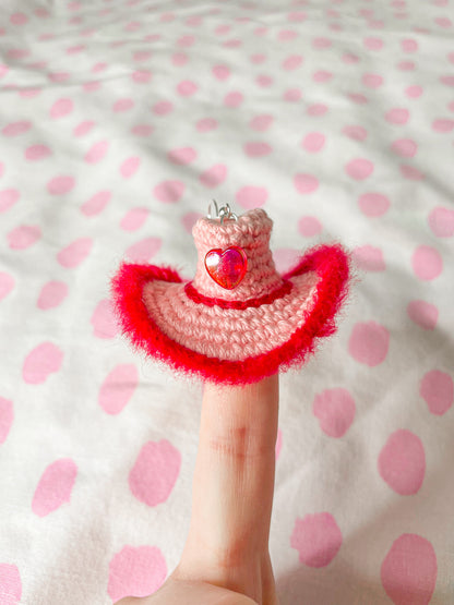 One cowboy hat shaped earring in pink and red sitting on top of someone's finger as if it's wearing a hat.