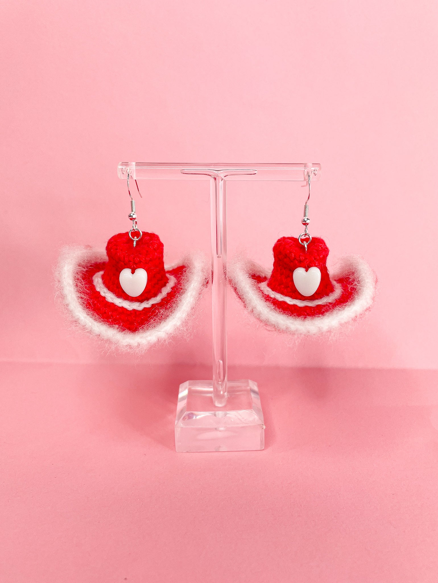 Pair of earrings shaped like cowboy hats in red and white hanging on an earring stand.