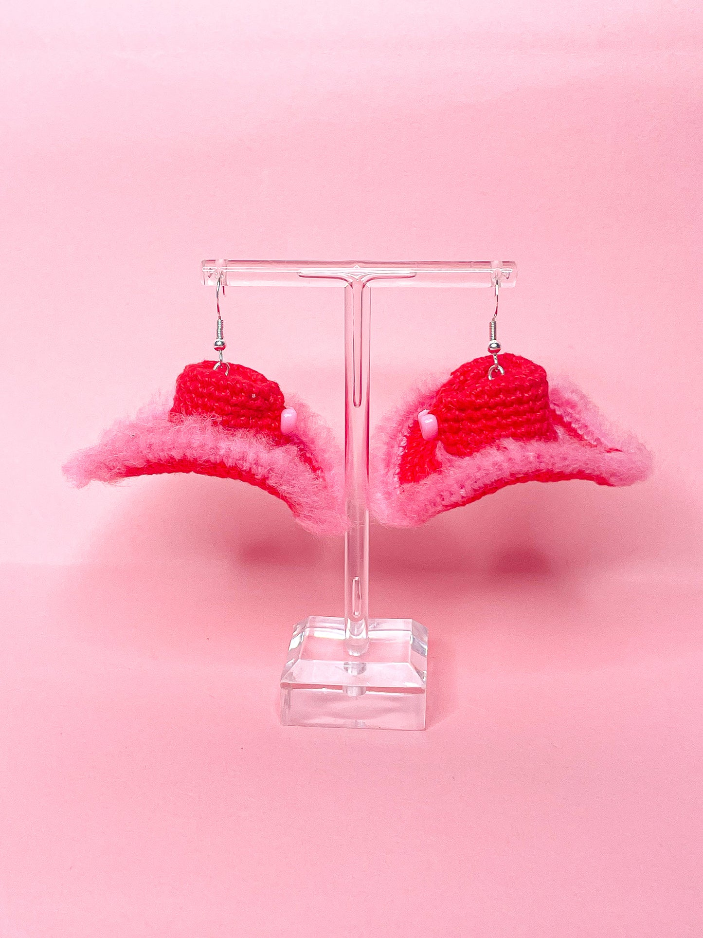 Side view of a pair of crochet earrings in red and pink hanging on an earring stand.