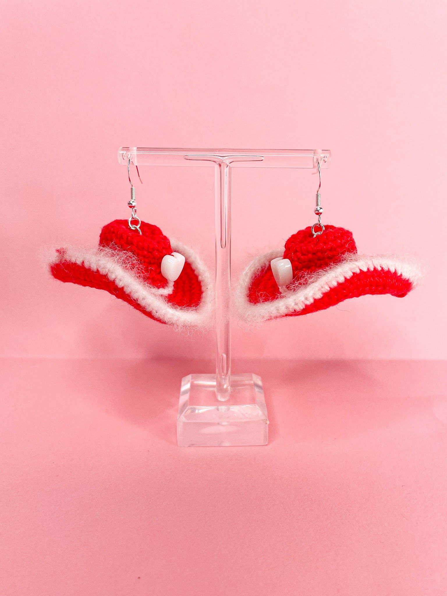 Side view of a pair of red and white earrings shaped like cowboy hats hanging on an earring stand.