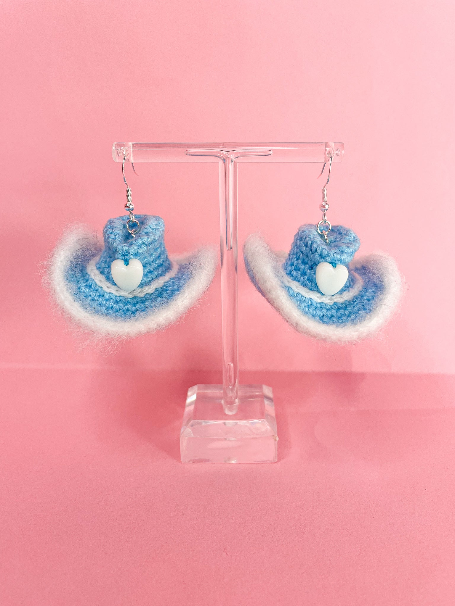 A pair of crochet earrings shaped like cowboy hat earrings in baby blue hanging on an earring stand.