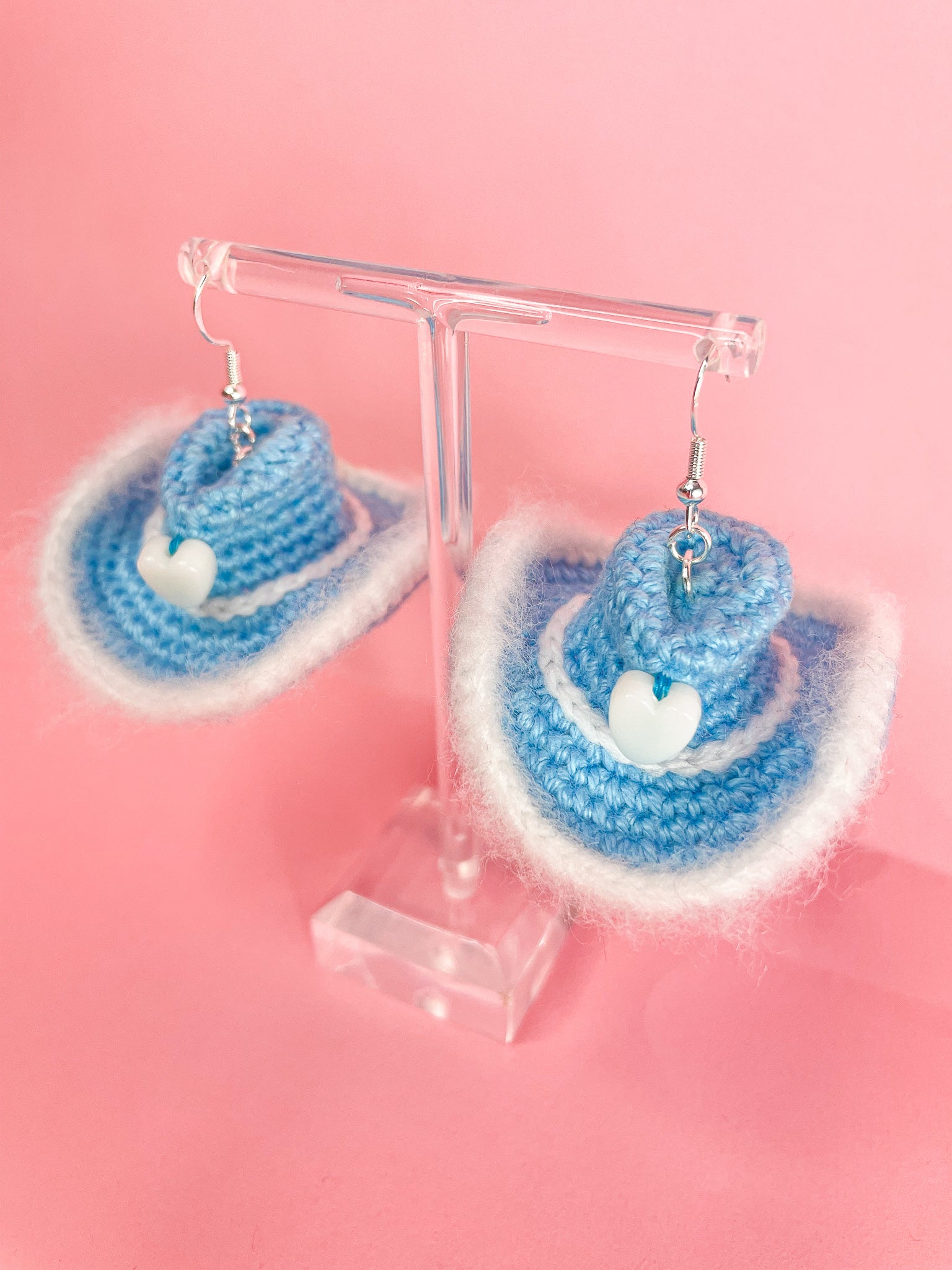 Above view of a pair of baby blue earrings shaped like cowboy hats hanging on an earring stand.