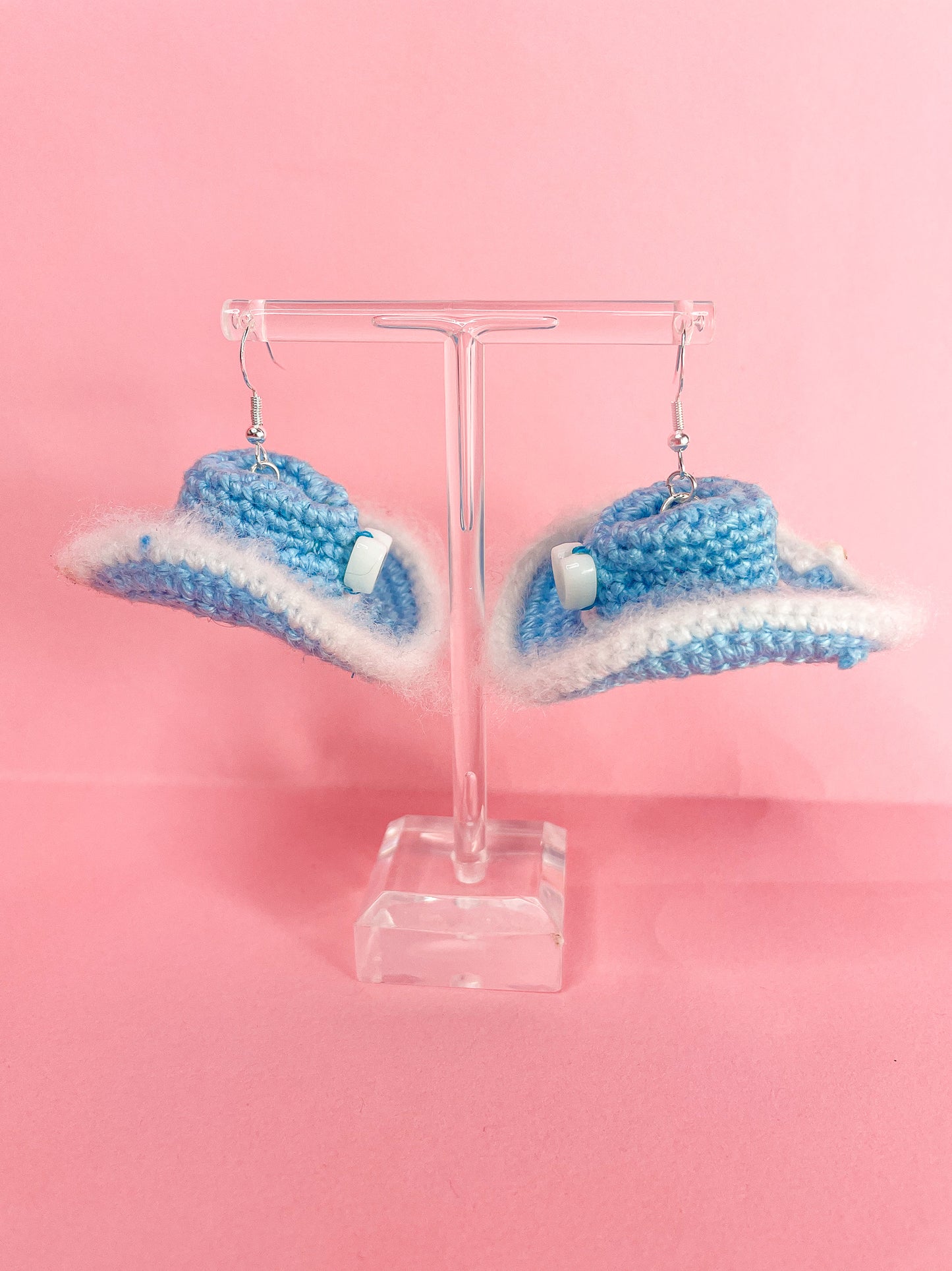 Side view of a pair of baby blue crochet cowboy hat earrings hanging on an earring stand.