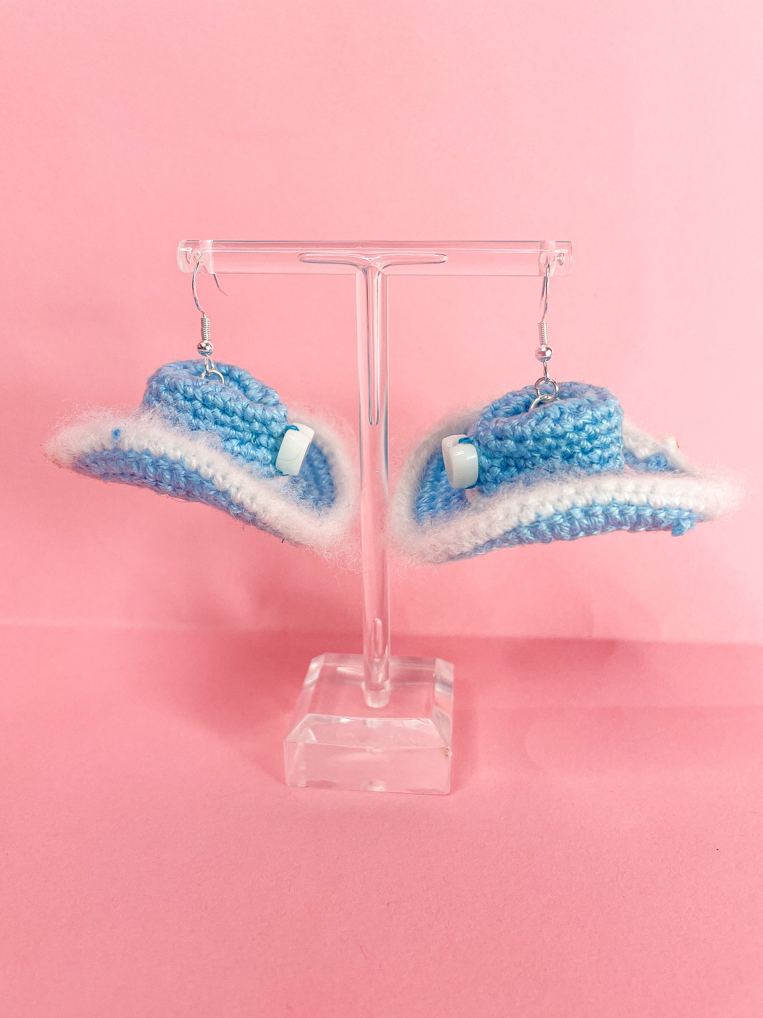 Side view of a pair of baby blue crochet cowboy hat earrings hanging on an earring stand.