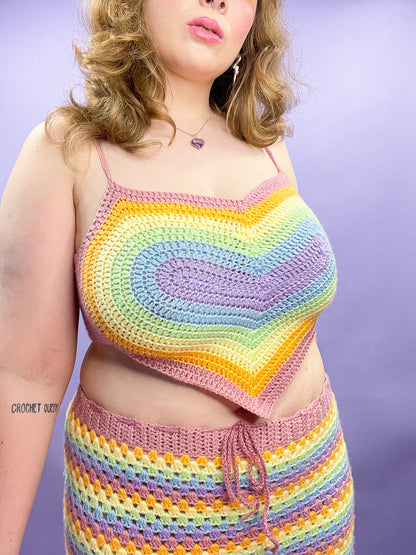 Close view of a woman wearing a crochet heart crop top with a pastel rainbow design and a matching skirt with a lilac heart necklace.