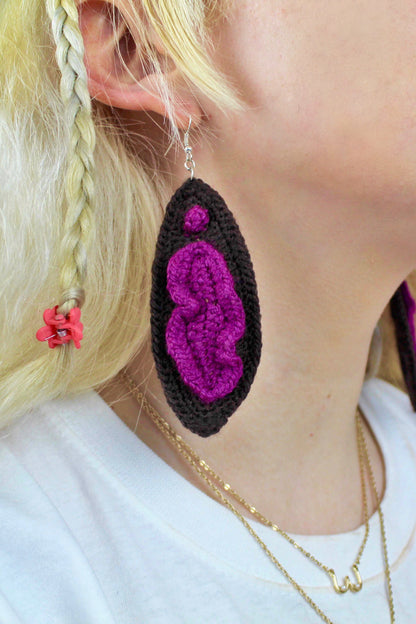 Close view of one dark brown earring shaped like a vulva worn by a woman.