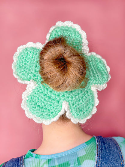 Close view of woman wearing a flower shaped scrunchie in mint green with white frilly edges around it.