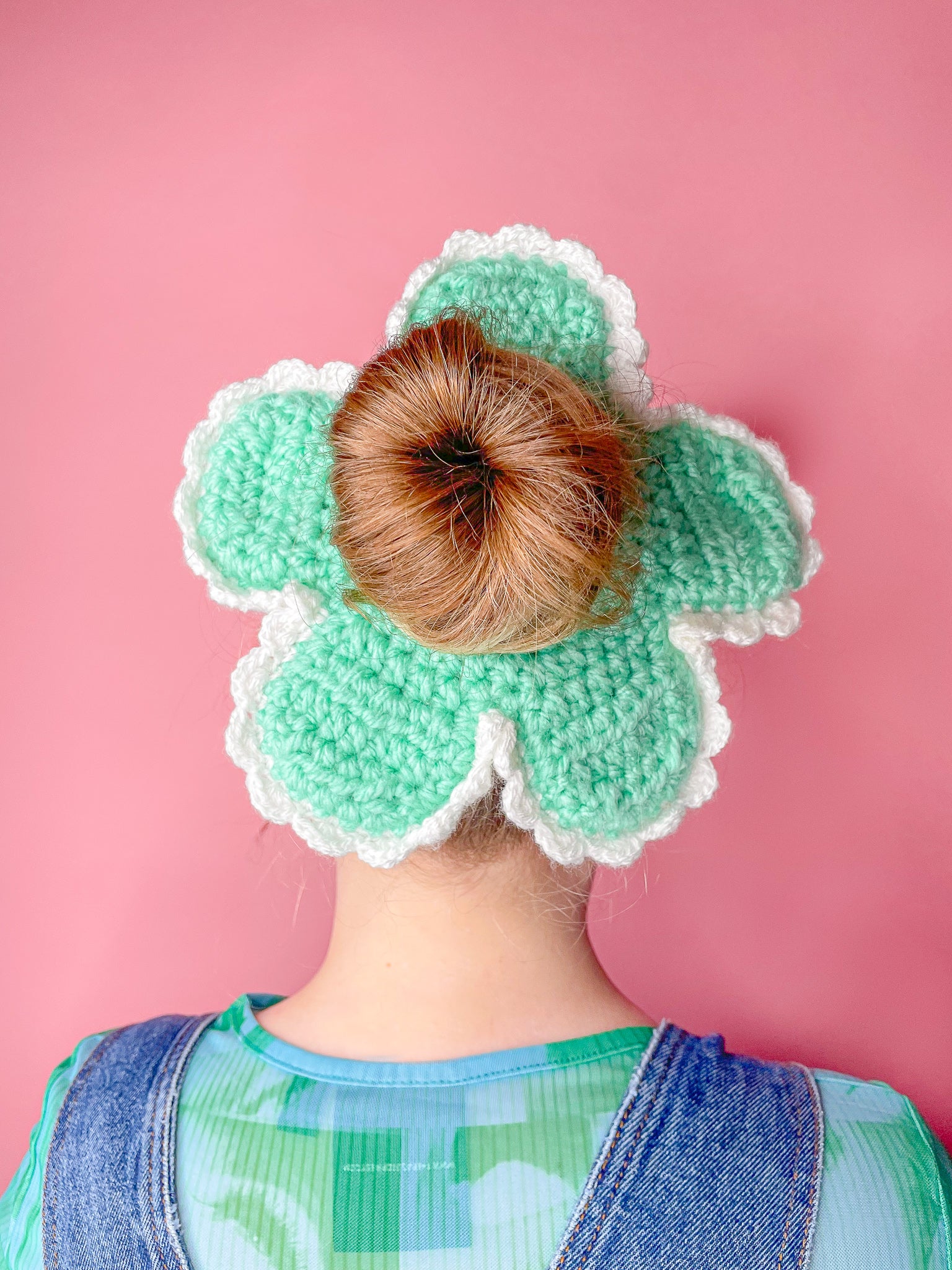 Back view of a woman wearing a crocheted scrunchie shaped like a flower in green with a matching top and denim dungarees.