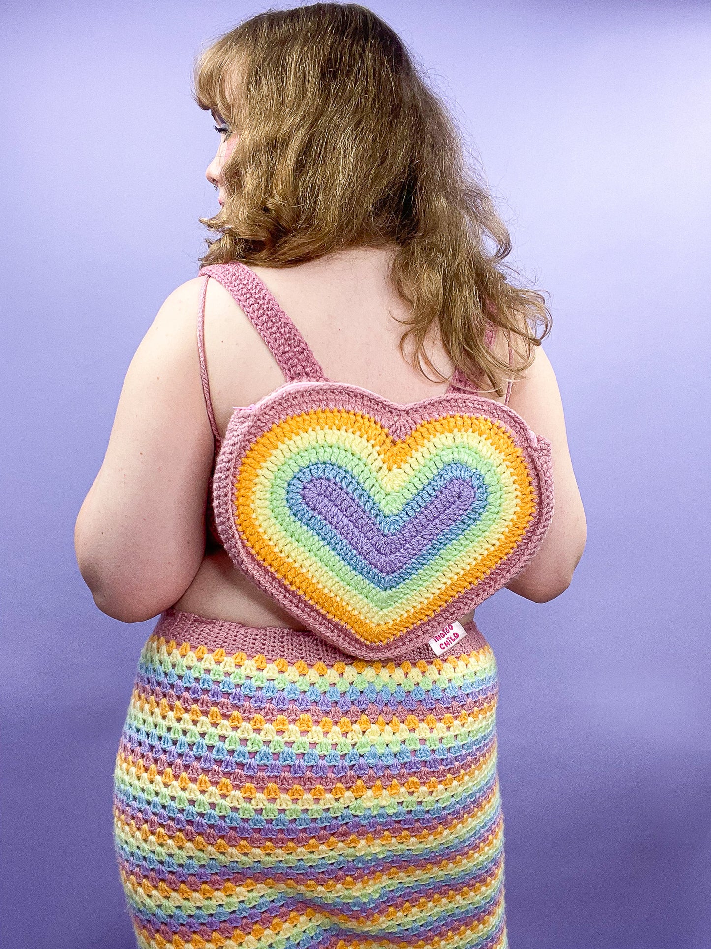 Back view of a woman wearing a heart shaped backpack with a pastel rainbow design, paired with a matching skirt.