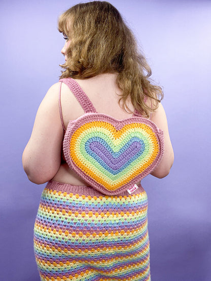 Back view of a woman wearing a heart shaped backpack with a pastel rainbow design, paired with a matching skirt.