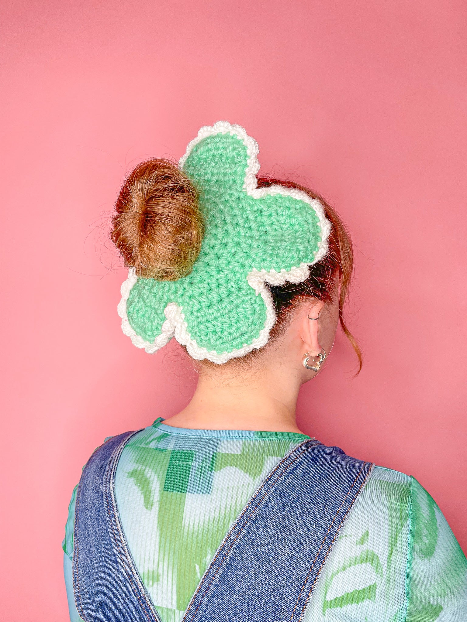 Side view of a woman wearing a crocheted scrunchie shaped like a daisy in mint green with a matching mesh top and denim dungarees.