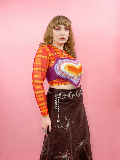 Side view of woman posing wearing a lesbian flag heart crop top with an orange top underneath and matching lesbian flag eyeshadow.