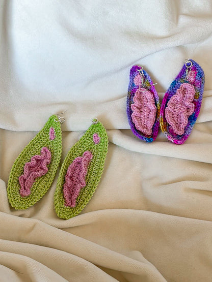 Two pairs of crocheted earrings that look like vaginas in brown and multicoloured, lying on a white background.